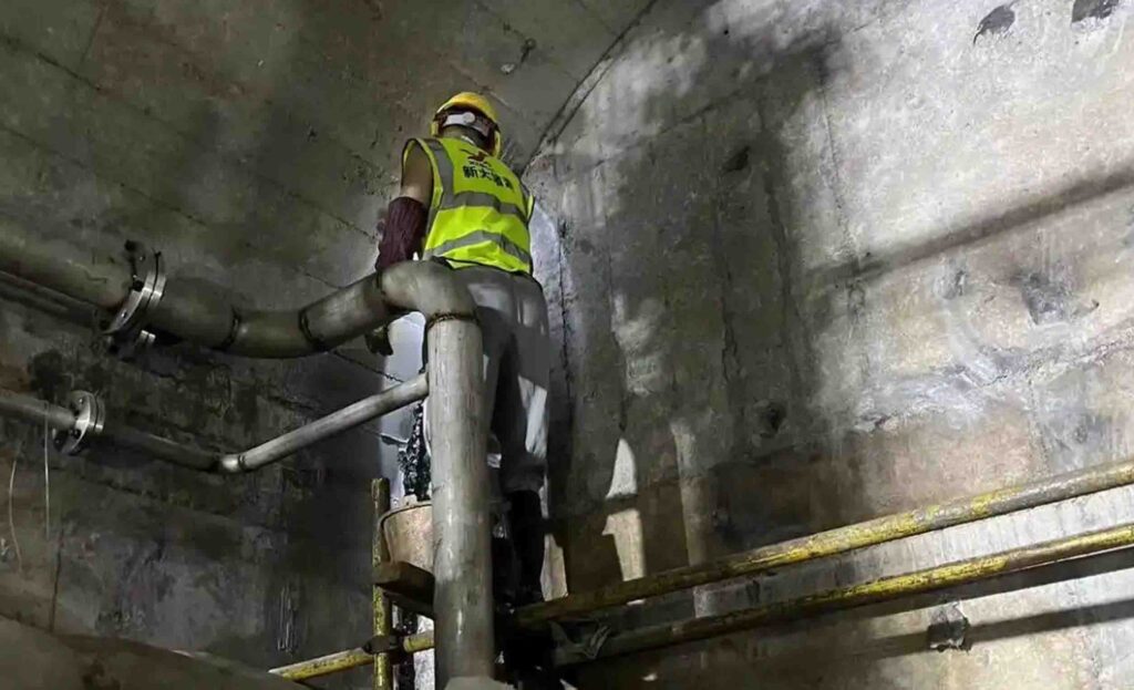 Grouting construction site with injection pump hoses and worker drilling boreholes for soil stabilization and water cutoff