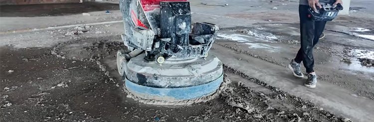 Concrete grinding machine with diamond abrasives leveling industrial warehouse floor during surface preparation