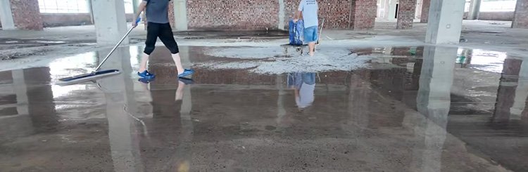 Worker spraying liquid concrete densifier on industrial floor with low pressure sprayer